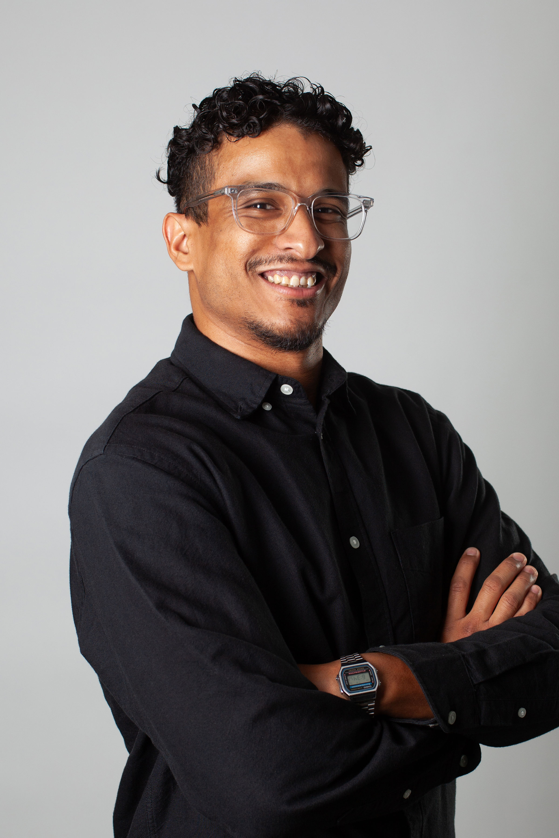 Auto-generated description: A person wearing glasses and a patterned white shirt is smiling against a plain background.
